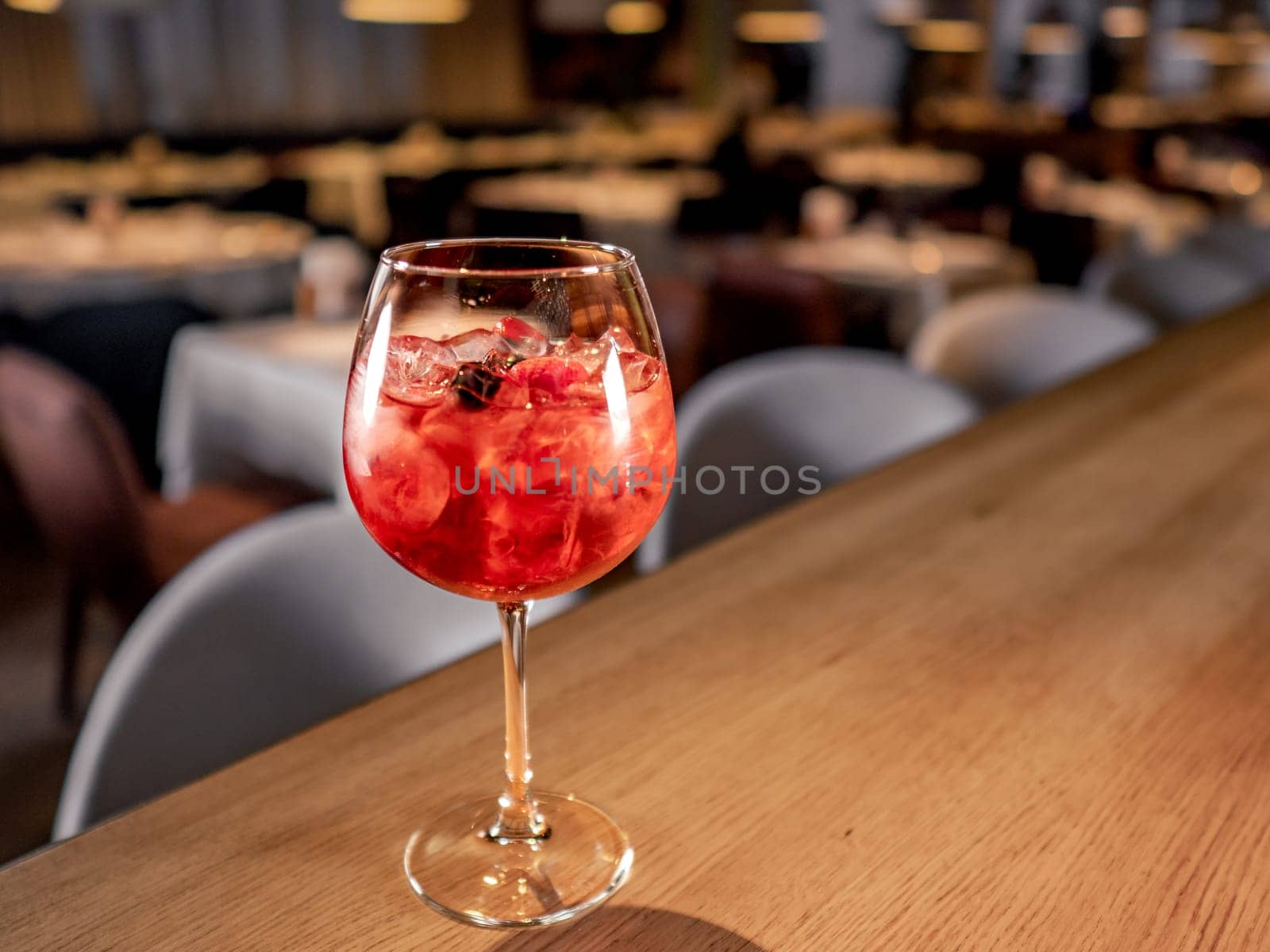 Glass of orange aperol spritz cocktail. Aperitif pink cocktail in wine glass with sparkling wine, syrup and ice cubes on bar counter in restaurant interior background, copy space