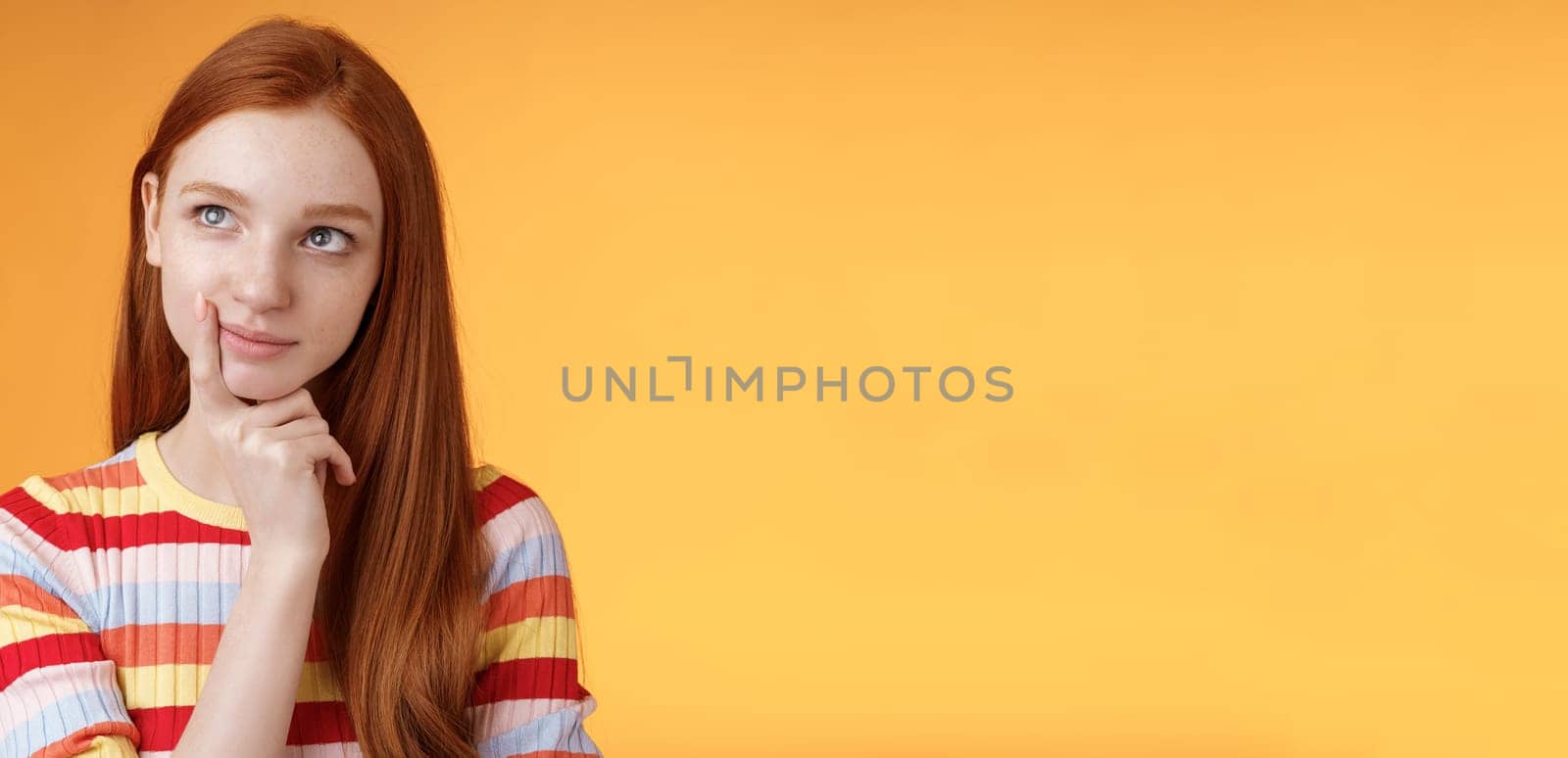 Creative thoughtful young smart redhead female student thinking ideas project look upper left corner dreamy touching lip pondering choice, taking important decision what order, orange background.