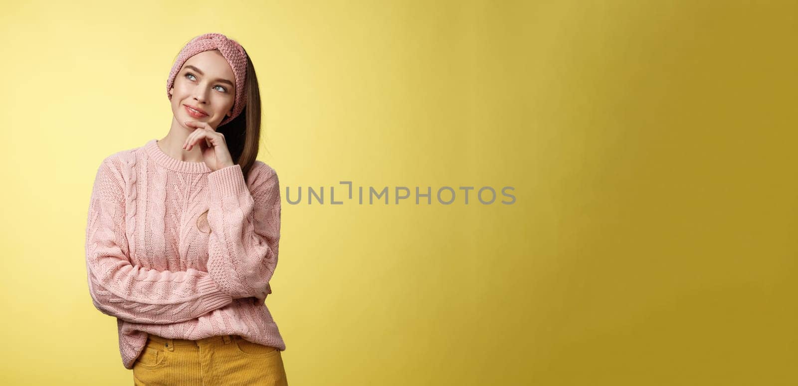 Dreamy attractive and stylish schoolgirl in knitted warm sweater, headband, thinking as smiling satisfied and devious having idea, looking at upper left corner thoughtful, daydreaming, planning.
