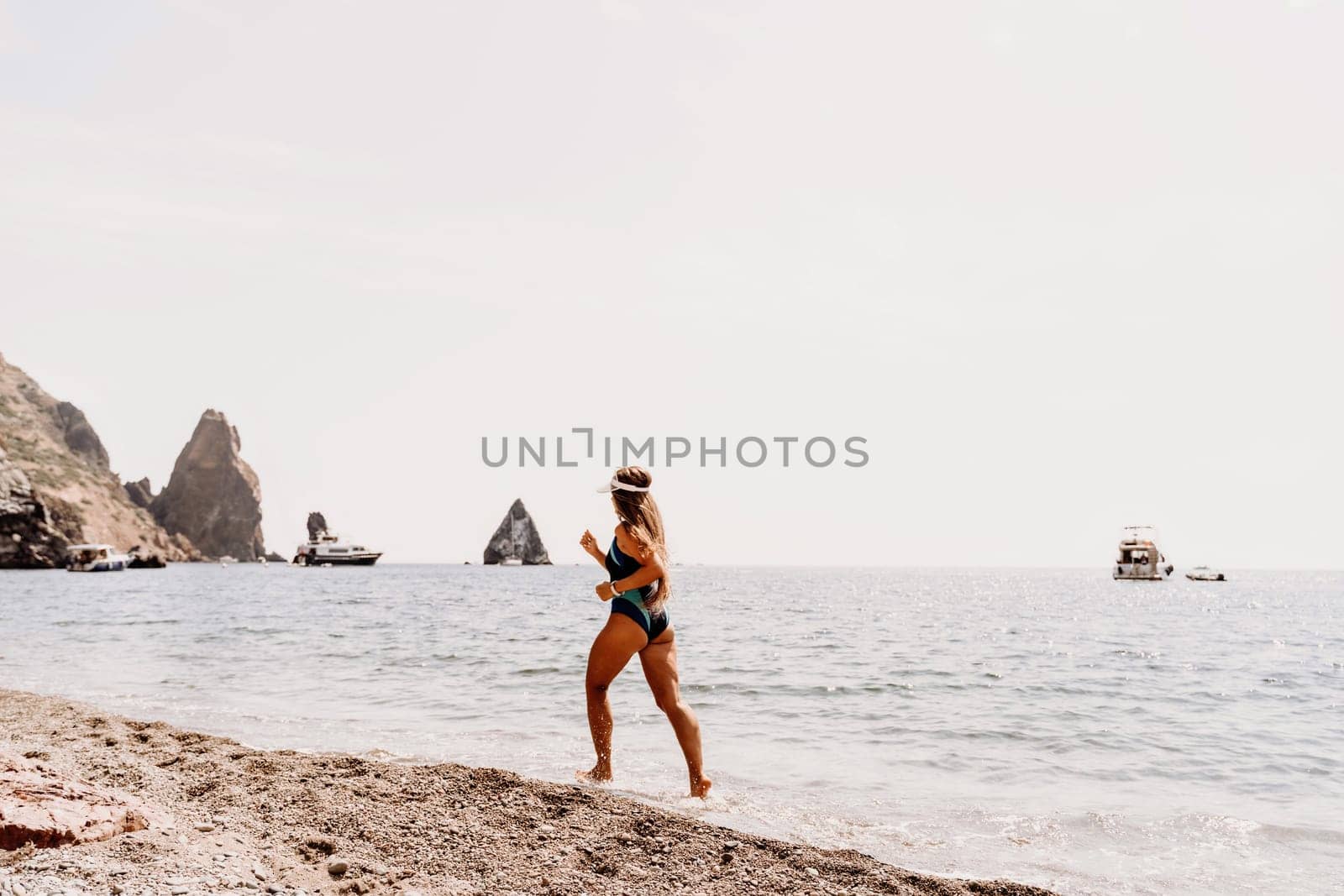 Woman beach vacation photo. A happy tourist in a blue bikini enjoying the scenic view of the sea and volcanic mountains while taking pictures to capture the memories of her travel adventure