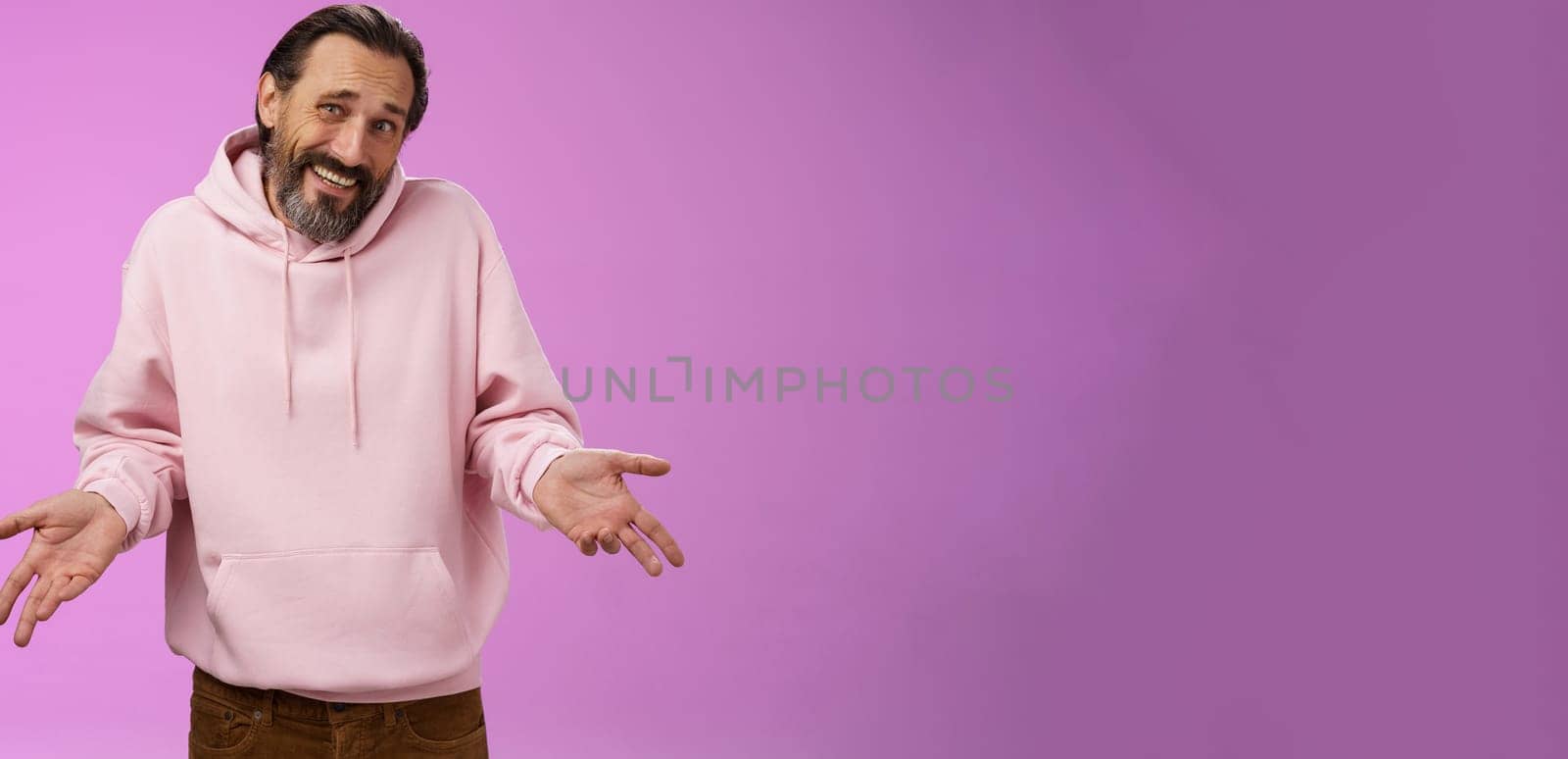 Portrait doubtful unsure awkward mature man shrugging spread hands sideways clueless cringing frowning hesitant cannot say yes no facing hard decision standing perplexed purple background.