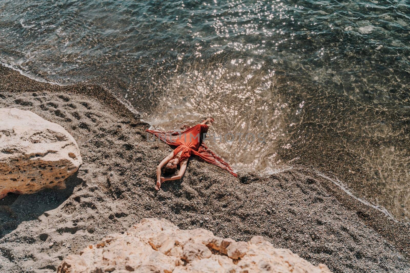 Woman red dress sea. Female dancer in a long red dress posing on a beach with rocks on sunny day.