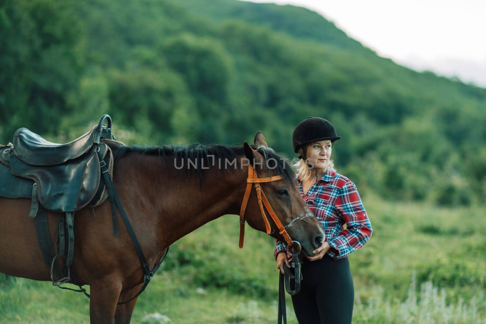 Happy blonde with horse in forest. Woman and a horse walking through the field during the day. Dressed in a plaid shirt and black leggings