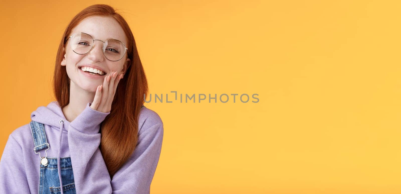 Charismatic happy tender redhead smiling european girl 20s glasses hoodie denim overalls having fun enjoying summer holidays chilly evening laughing joyfully touch pure clear skin, orange background by Benzoix