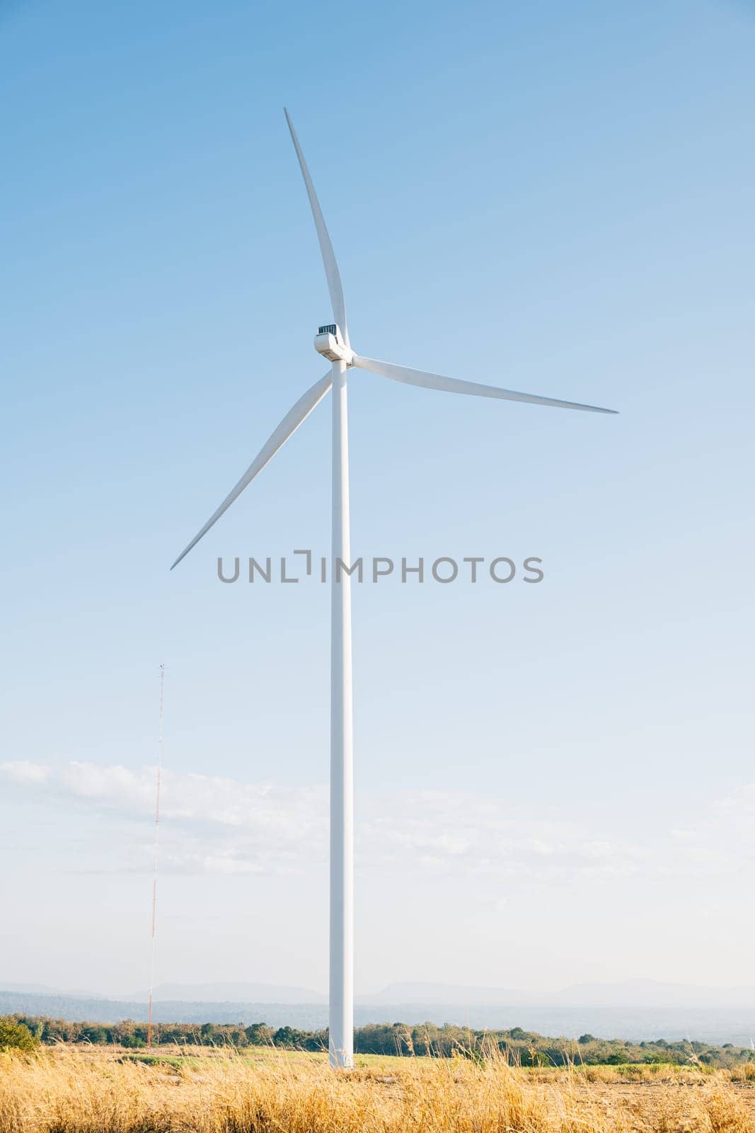 Atop a mountain windmill farm turbines turn in sync with nature generating clean energy. Modern wind technology supporting sustainable development under a serene blue sky.