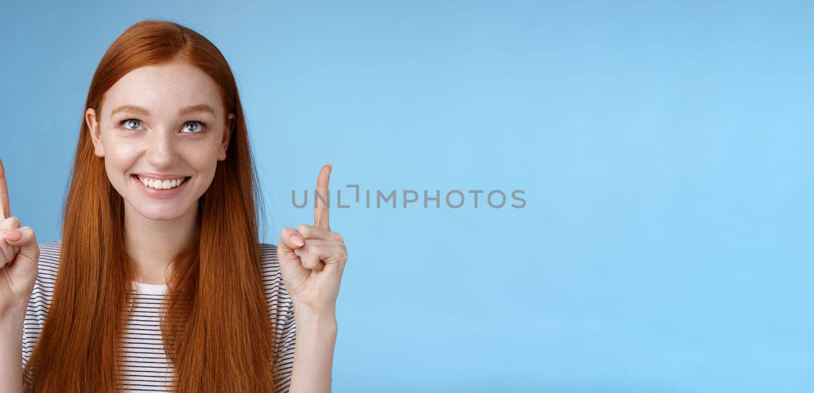 Cheerful curious amused happy entertained redhead pretty girl gazing pointing up smiling approval like interesting product watching perfomance enjoy cool holiday promos, standing blue background.