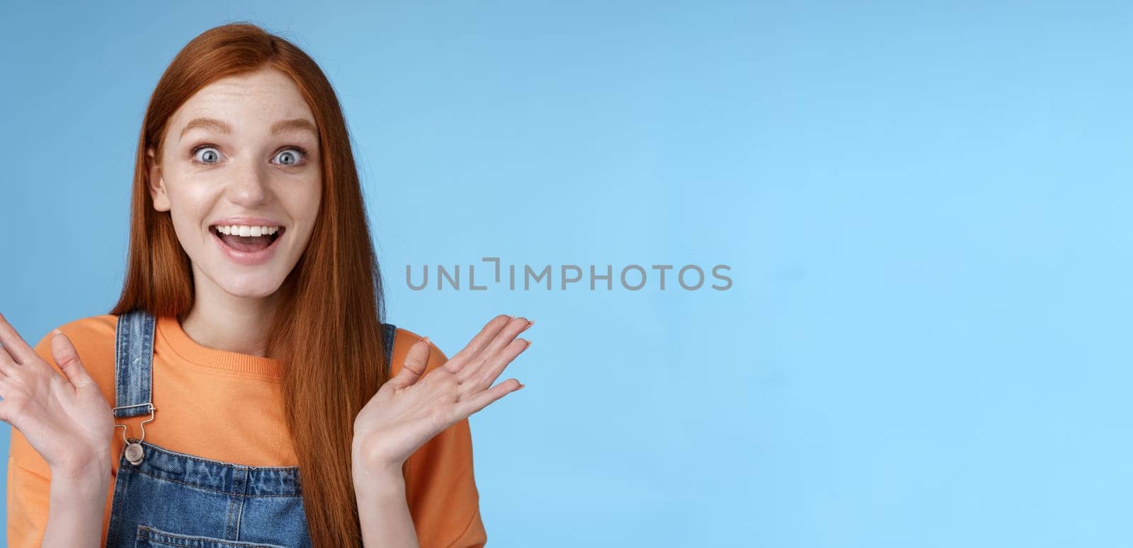 Surprised delighted happy friendly-looking amused redhead female friend learn incredible good news congratulating girlfriend fascinated wide eyes camera joyfully clap hands amazed, blue background by Benzoix