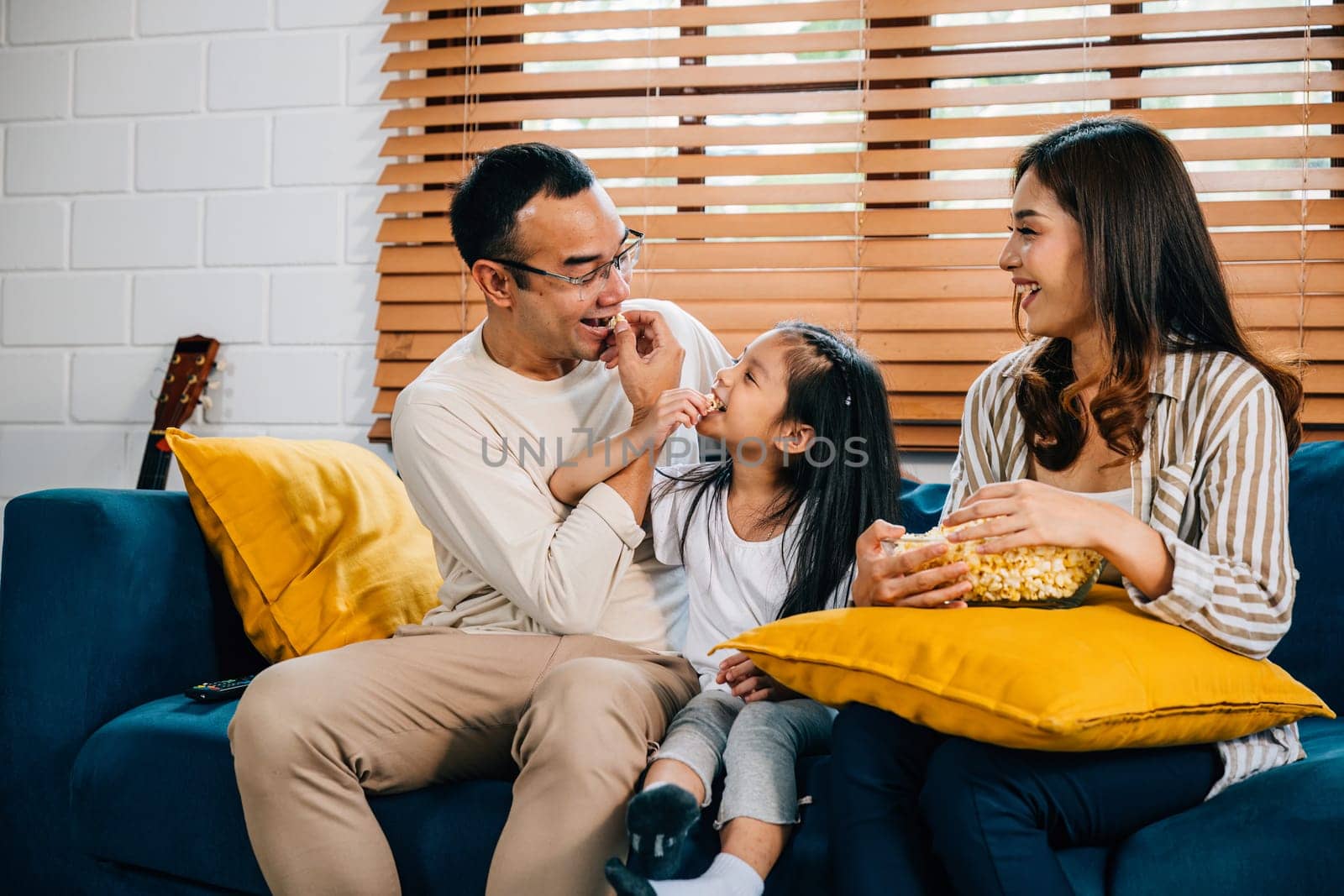 A smiling family with popcorn gathers in living room watching TV together. They are enjoying candid moments of togetherness bonding and relaxation during their quality time at home.