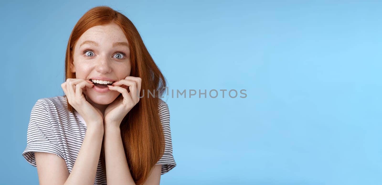 Excited amazed attractive redhead girl blue eyes look fascinated affection smiling desire bite fingernails eager feel astonished cannot wait bite tasty food, standing blue background thrilled by Benzoix