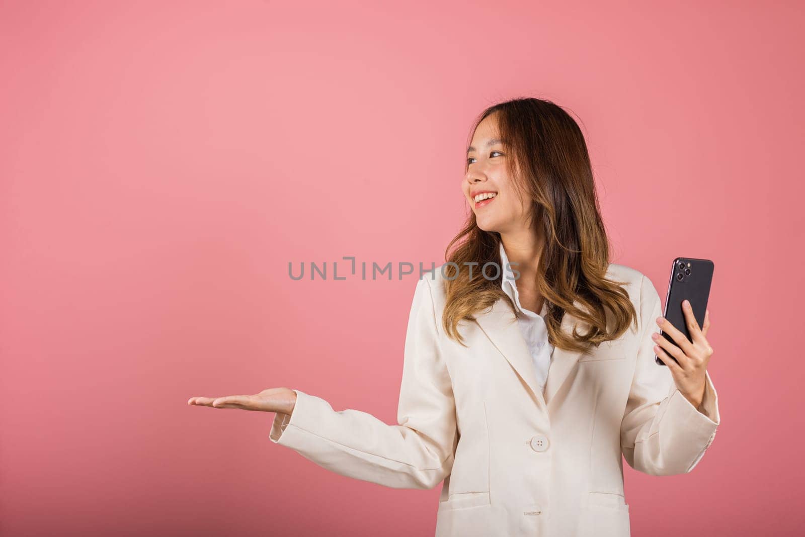 woman excited holding mobile phone blank screen presenting product with palm of hand at empty by Sorapop