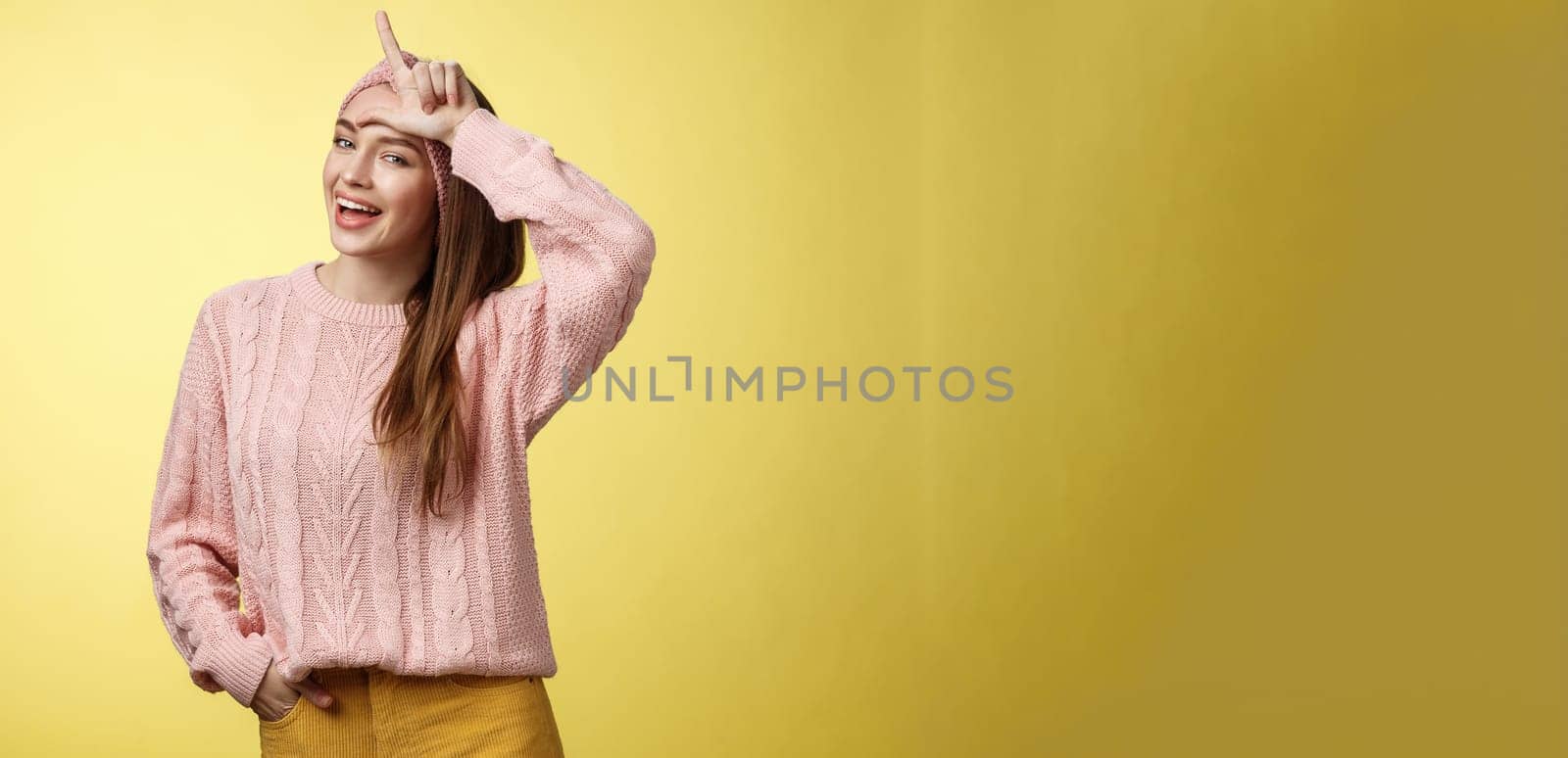 Attractive triumphing arrogant and confident cute glamourous woman in knitted sweater, headband showing l letter on forehead, loser sign and laughing over lost team, mocking having fun. Copy space
