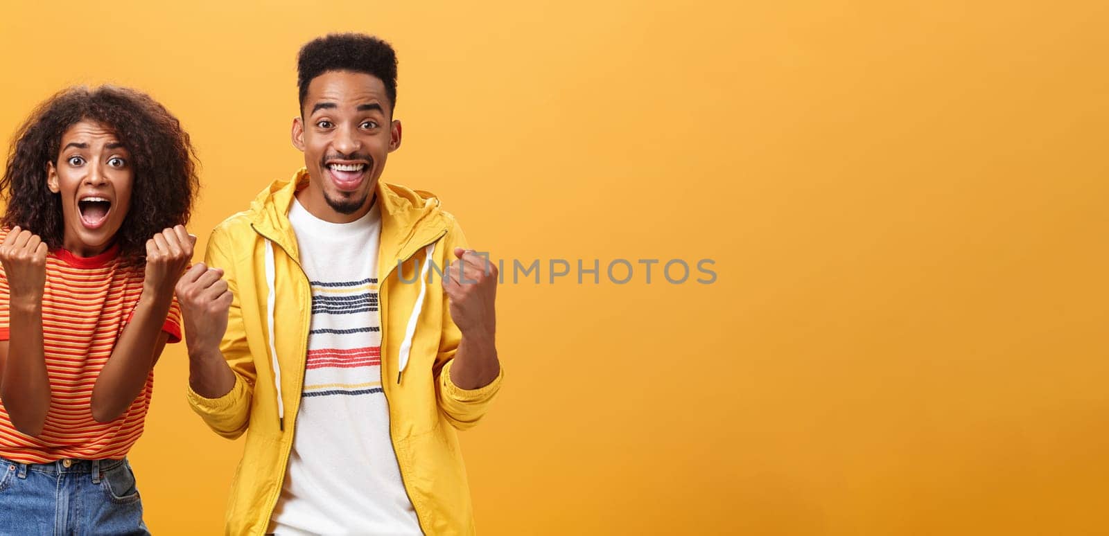 Two friends cheering and supporting mate on competition yelling joyfully clenching fists in supportive geture smiling broadly waiting with amazement and excitement for win and victory. Lifestyle.