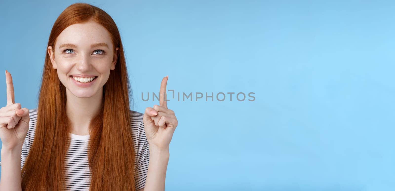 Amused excited happy smiling redhead girl look pointing up grinning gladly watching awesome open air perfomance standing joyfully showing cool thing indicating product, blue background by Benzoix