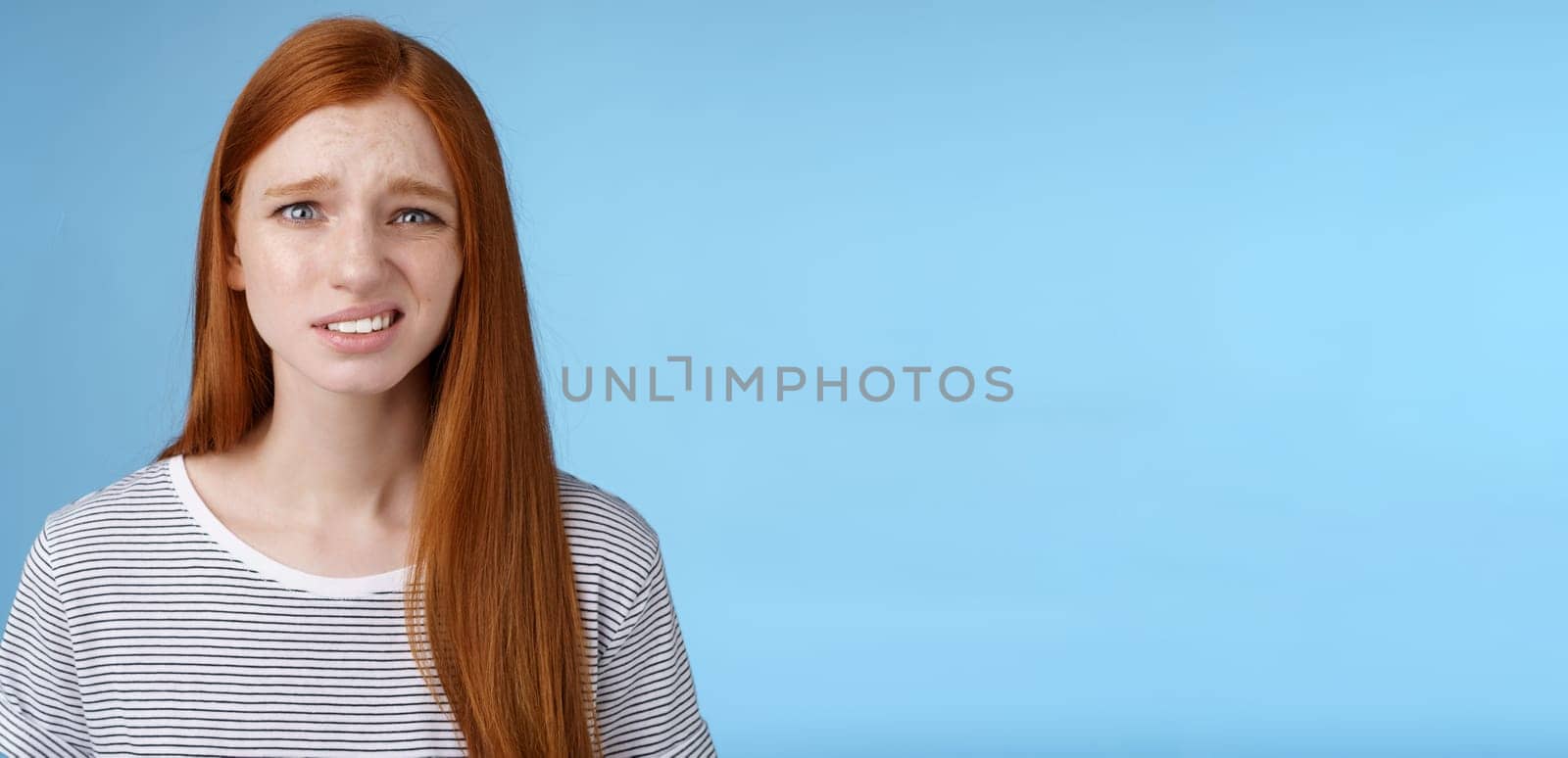Displeased young awkward redhead girl cringe full disbelief smirking frowning confused look questioned doubtful hearing nuisance dumb story standing blue background uncertain by Benzoix