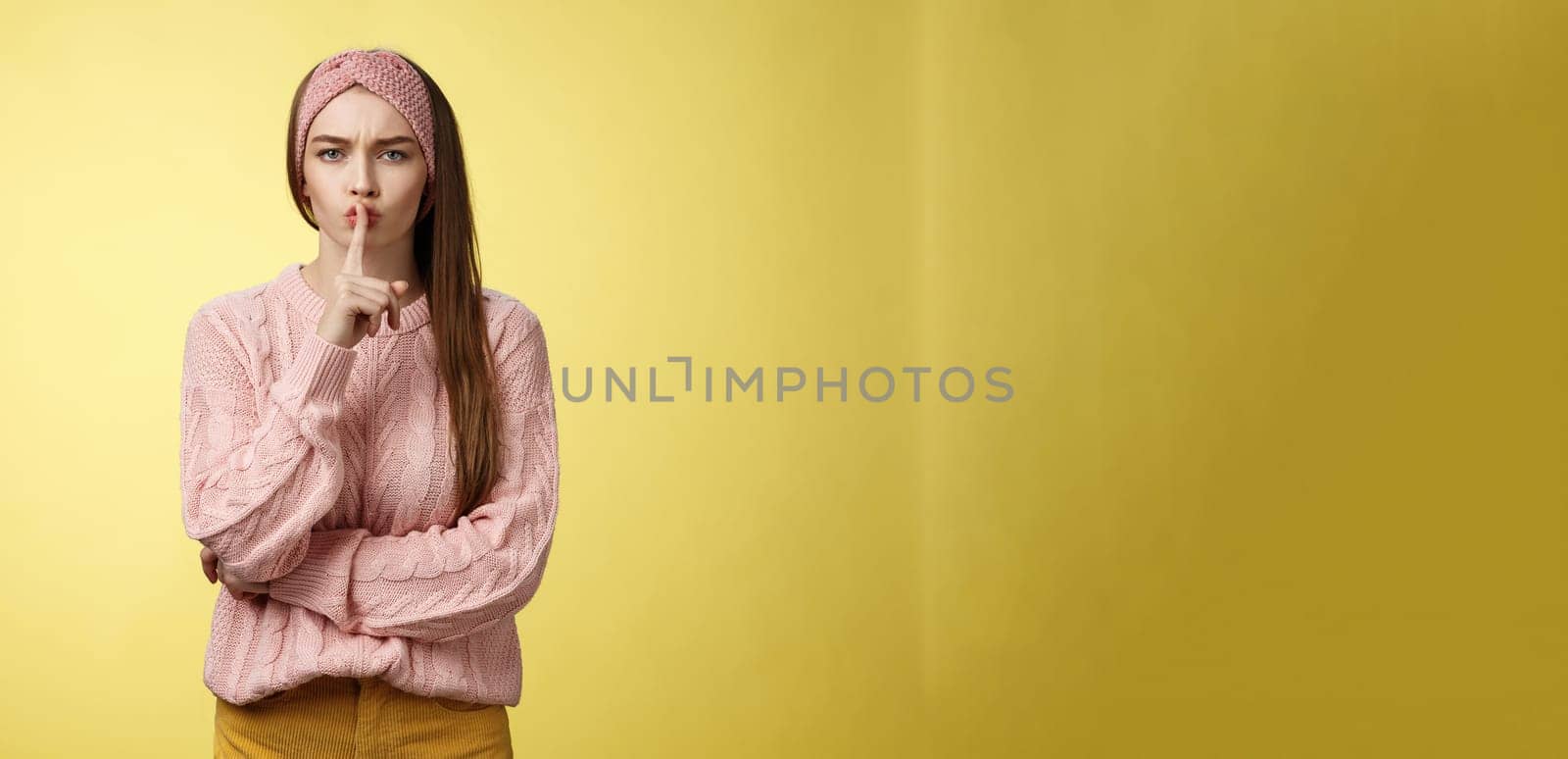 Keep mouth shut. Serious-looking bossy attractive young 20s woman in sweater, headband shushing making shhh gesture holding index finger on lips, gossiping, spread rumors over yellow background by Benzoix