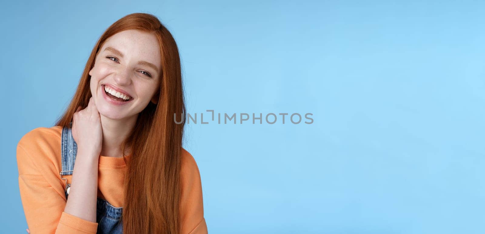 Carefree silly flirty young redhead girlfriend having fun enjoying lovely date summer evening laughing out loud smiling broadly tilting head touching neck shy blushing acting cute blue background by Benzoix