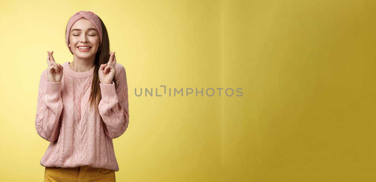 Girl wishing wellness wanting dream come true, cross fingers dreamy, close eyes waiting miracle, anticipating good news, posing excited and joyful against yellow background in knitted warm sweater by Benzoix