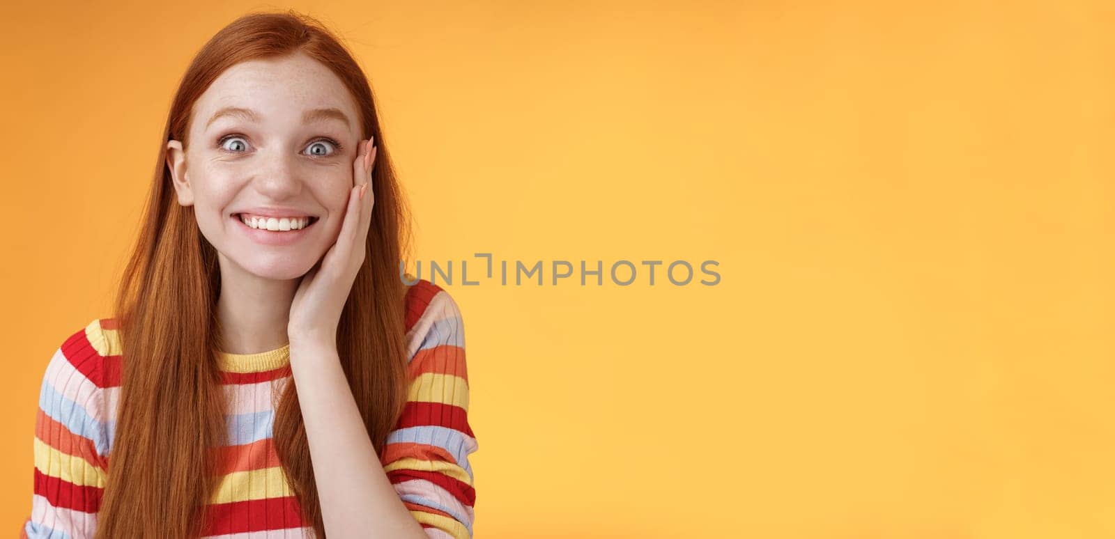 Cheerful glad excited attractive redhead girl blushing surprised feeling happy touch cheek pleased receive good news standing joyful thrilled get awesome chance, posing orange background by Benzoix