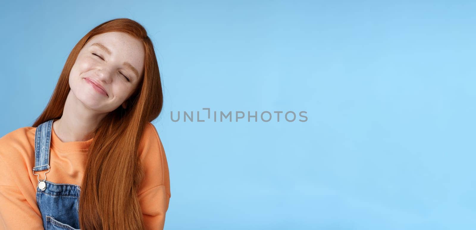 Dreamy kind silly redhead smiling happy girl straight long ginger hair daydreaming imagine romantic moment close eyes smiling delighted tilting head look joyful, standing blue background by Benzoix