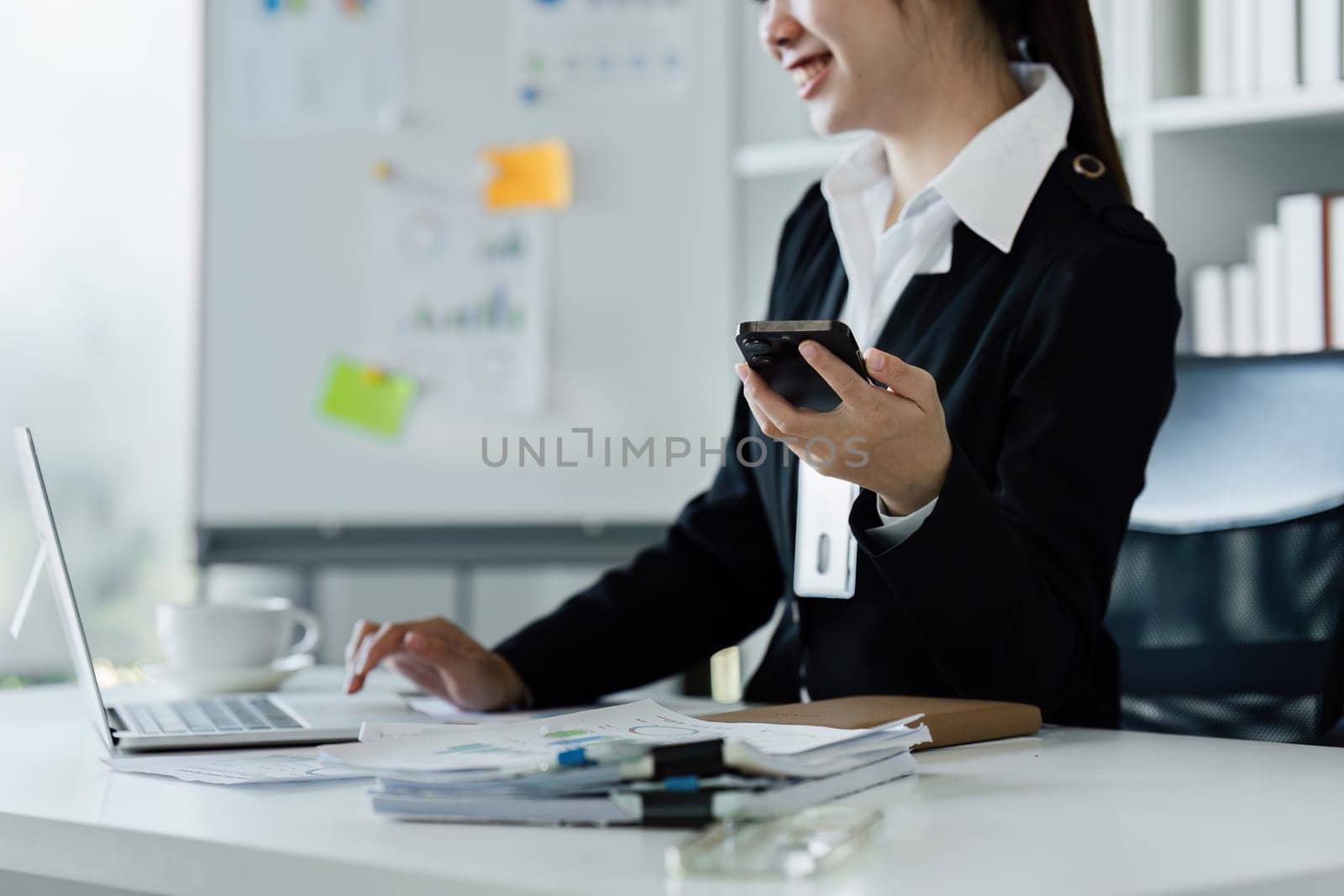 businesswomanman holding smartphone sitting in office. Manager using cell phone mobile app and laptop.