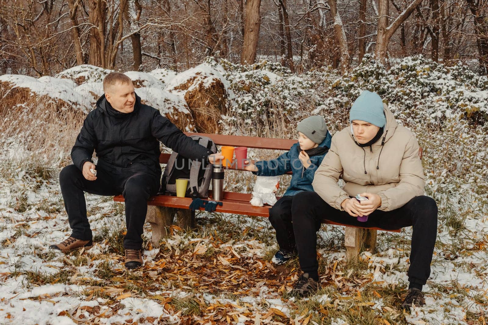 Snowy Park Serenity: Dad and Sons Share Treats and Smiles in a Winter Wonderland.