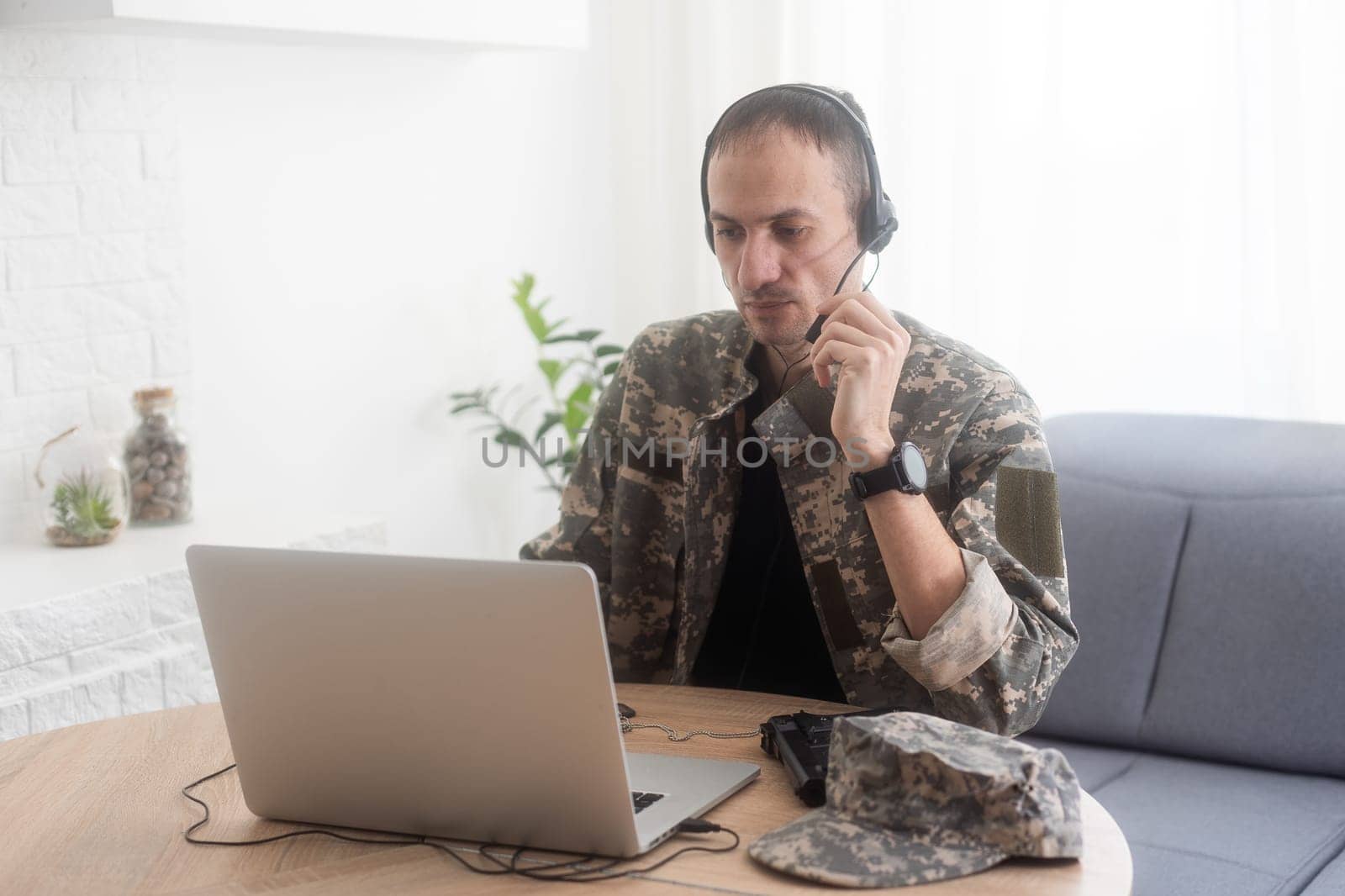 smiling soldier in headphones using laptop at kitchen table by Andelov13