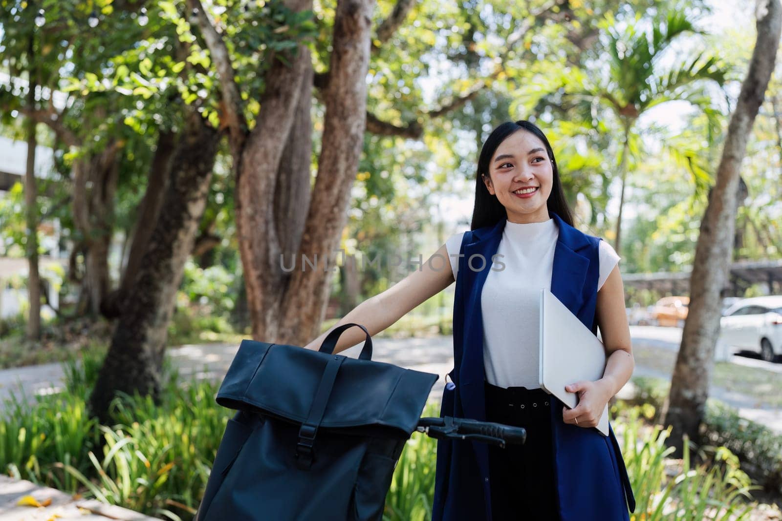 Young businesswoman sitting on stair in city park and using laptop for work hybrid. Bike to work eco friendly alternative vehicle green energy.