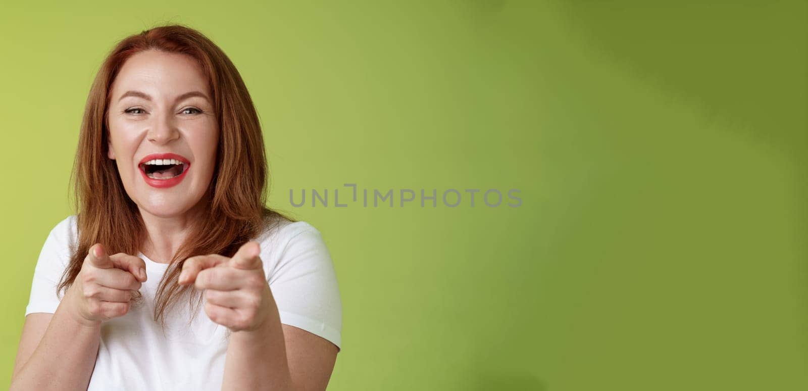 You did best. Friendly joyful enthusiastic redhead ginger middle-aged female pointing index fingers camera finger pistol gesture smiling broadly congratulate cheer coworker stand green background.