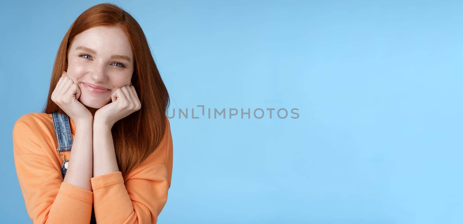Tenderness, wellbeing, beauty conept. Attractive young ginger girl pure skin blue eyes lean palms silly smiling camera look amused enthusiastic listen interesting stories gladly, blue background by Benzoix