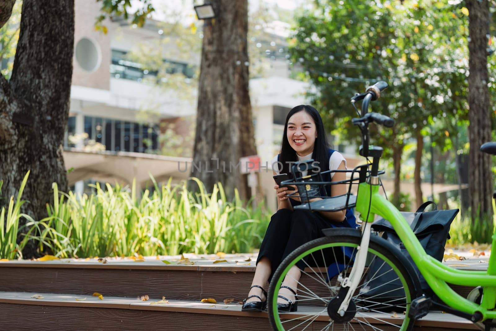 Asian young businesswoman bike to work for eco friendly green energy and use smart phone while commuting in city. Eco friendly by itchaznong