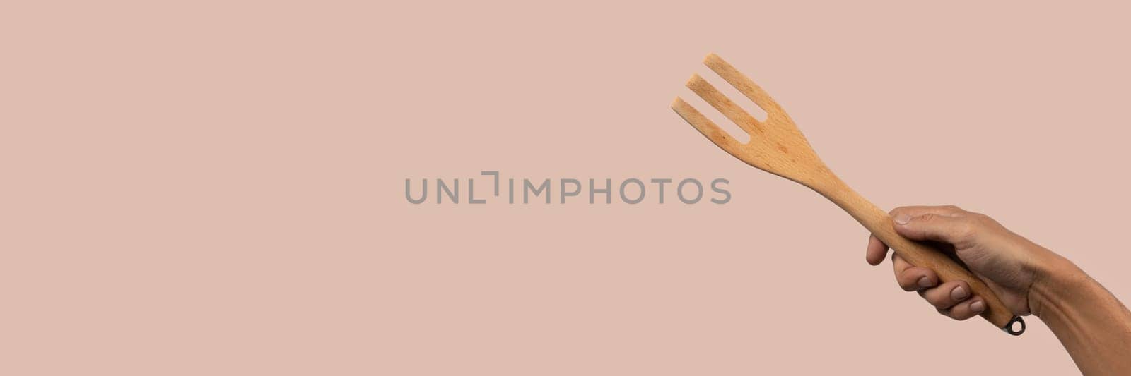 Hand holding wooden fork on dark pink background. High quality photo.