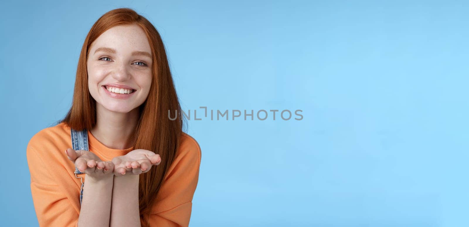 Cute tender kind young ginger girl giving all love you, hold something palms showing camera smiling delighted introduce present grinning romantic gesture send air kisses, blue background by Benzoix