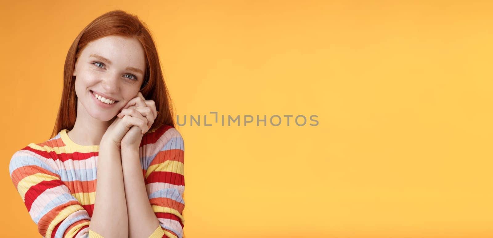 Romantic tender sensual attractive smiling redhead girlfriend melting heart feel warmth delighted lean palms grinning happily sweet gentle gift standing pleased orange background rejoicing thankful.