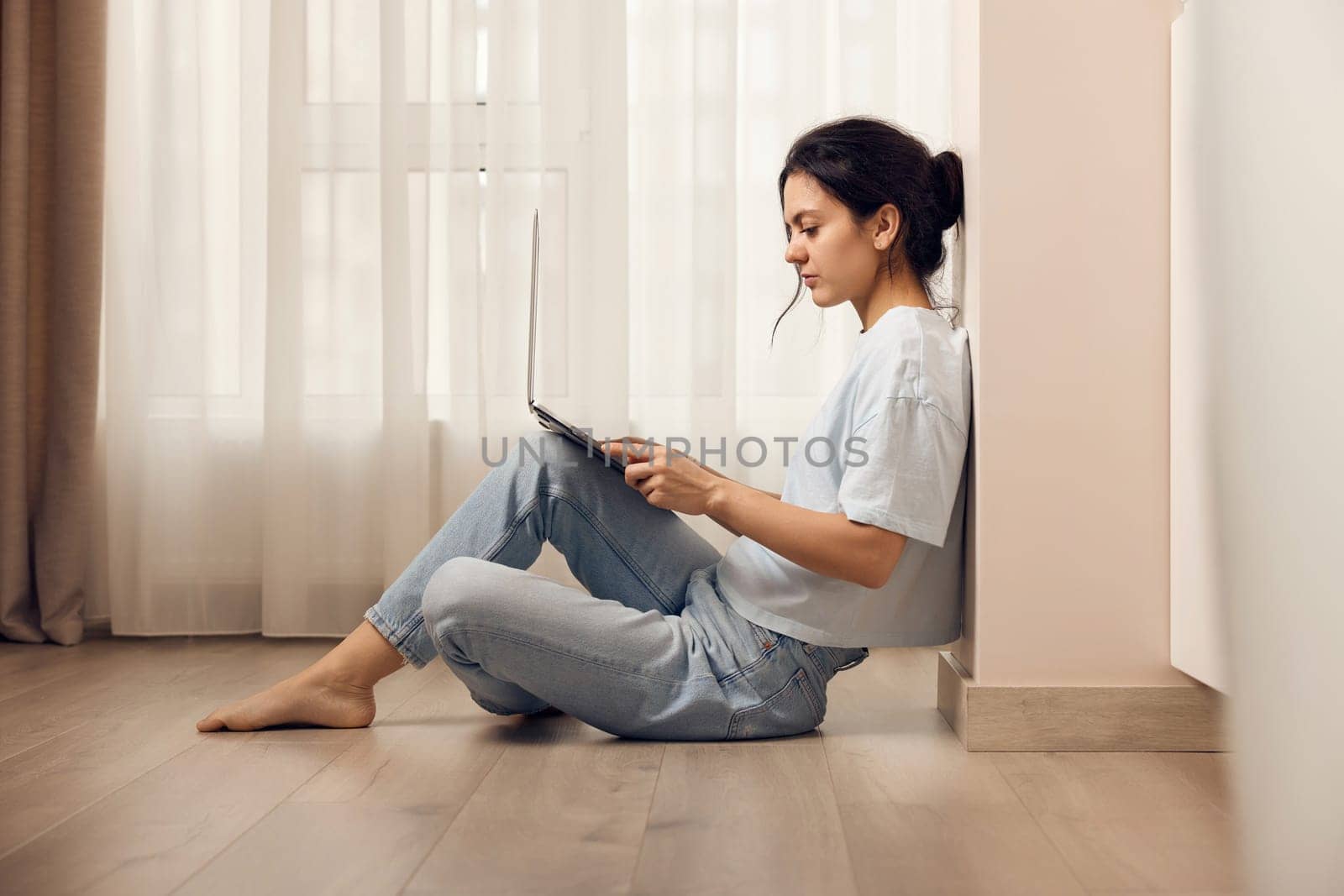 woman sitting on the floor and working on laptop at home by erstudio