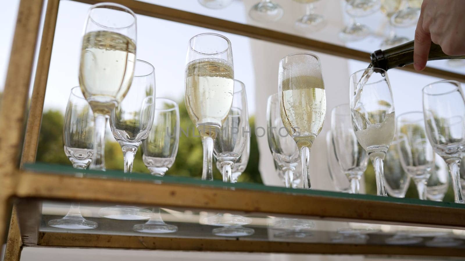 Open catering, champagne is poured into a glass, close-up. The waiter pours champagne into a glass. A bottle of sparkling champagne and glasses are poured into a glass at an outdoor wedding event.