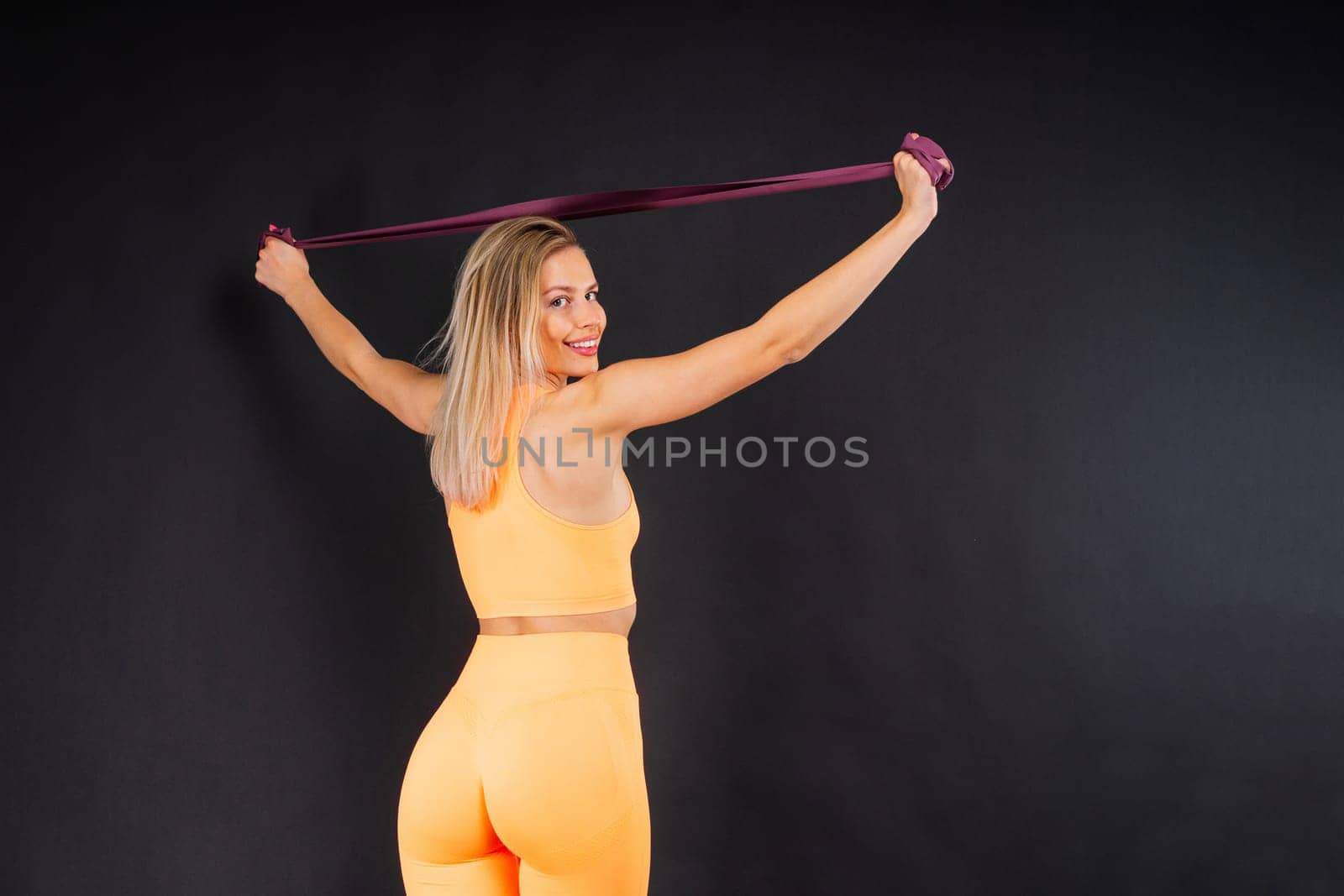 Sports woman in fashion sportswear exercising with elastic band in a studio