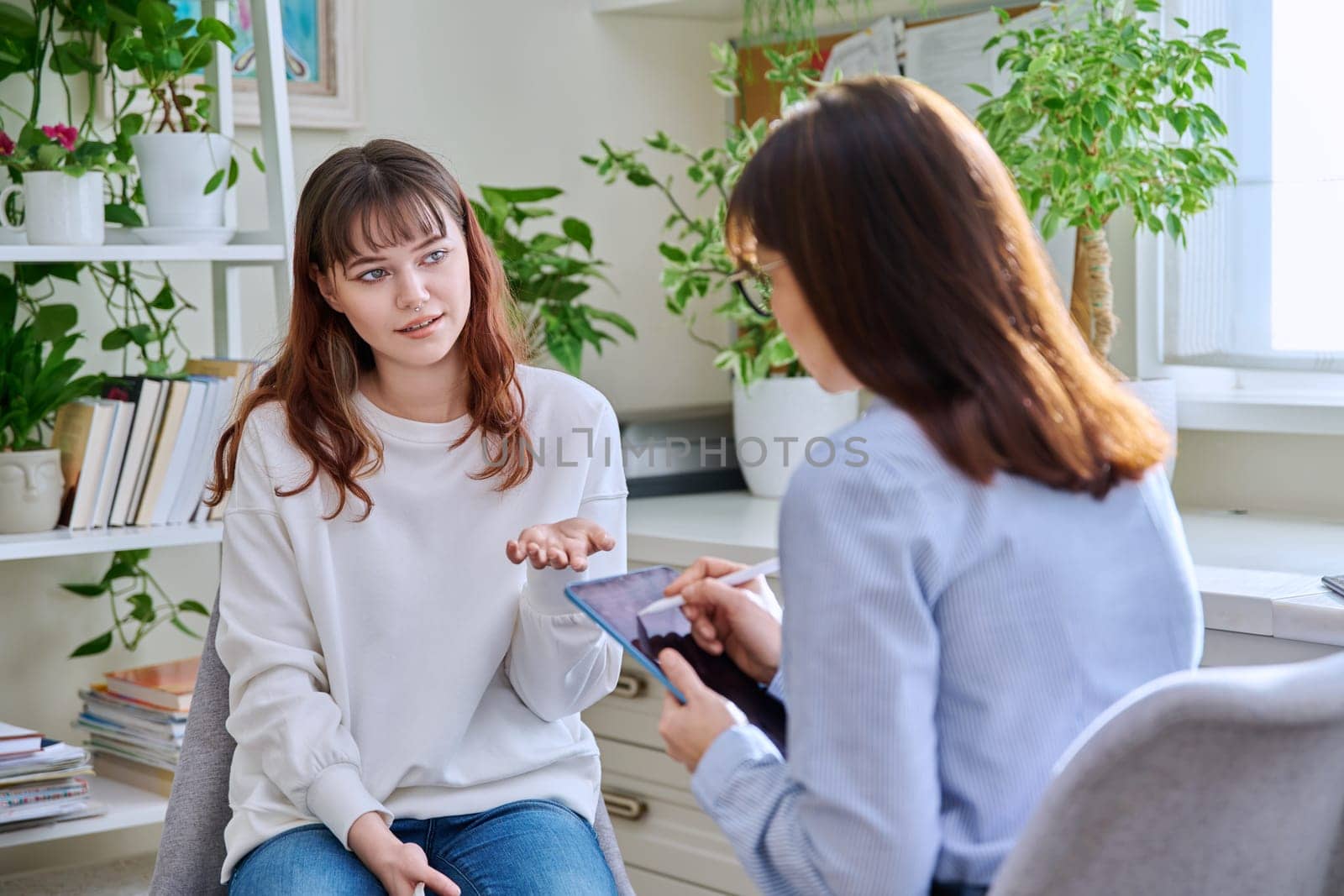 Teenage girl college student at therapy meeting with mental health professional social worker psychologist counselor sitting together in office. Psychology, psychotherapy, mental assistance support