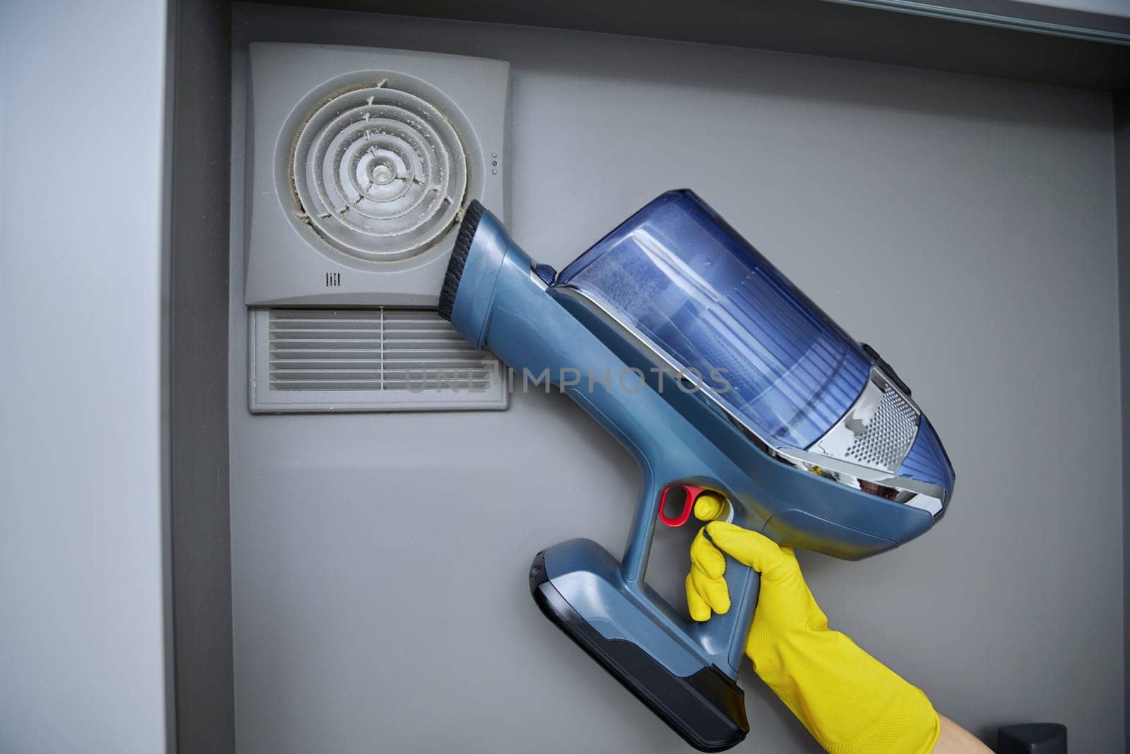 Cleaning wall-mounted hood ventilation grill in bathroom with vacuum cleaner by VH-studio