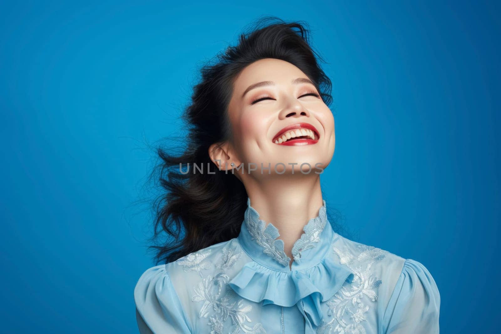 Portrait of a joyful woman laughing with closed eyes. Studio photography with blue background. Happiness and beauty concept. Design for advertisement, poster