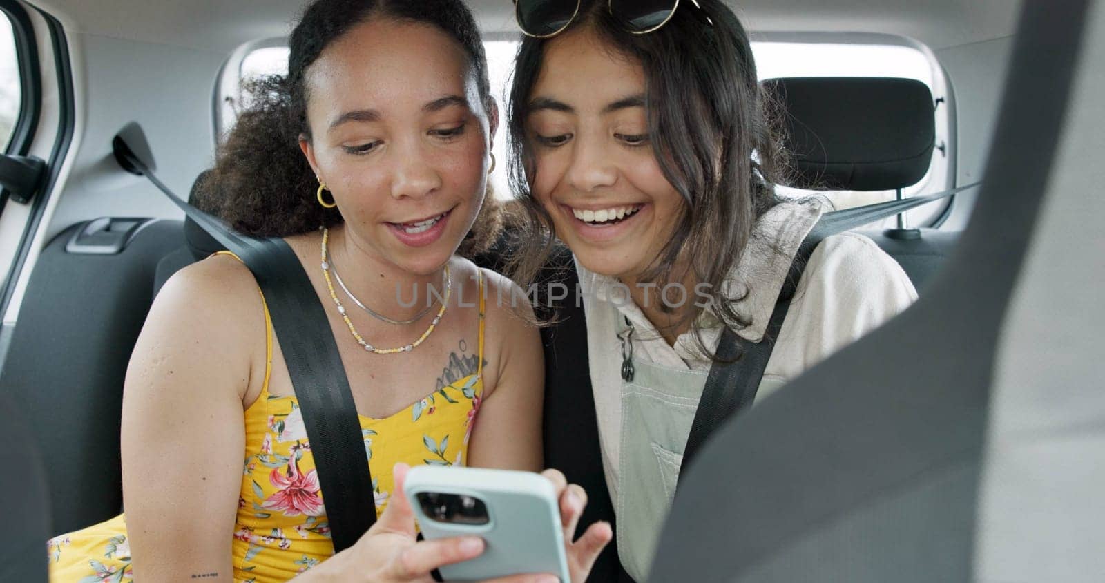 Happy friends, phone and car for road trip information, location search and social media. Young women reading on mobile app and talking of travel, holiday and transportation service with funny chat by YuriArcurs