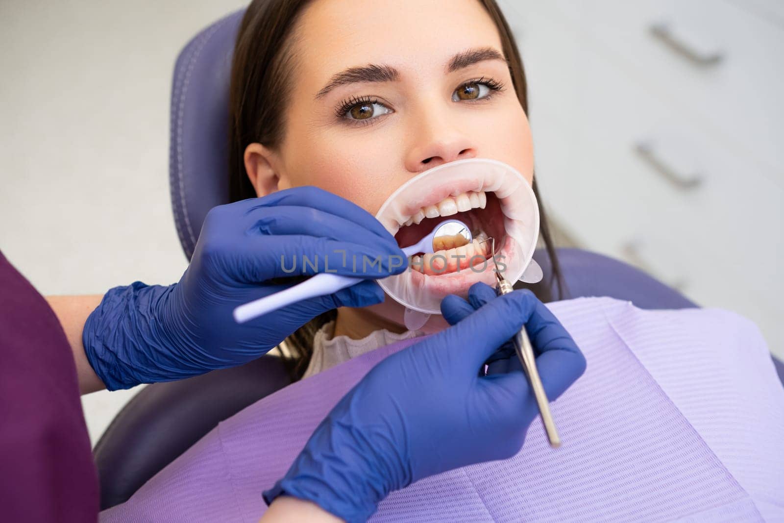 Portrait of young woman in dental clinic. Dentist in rubber gloves doing check up.