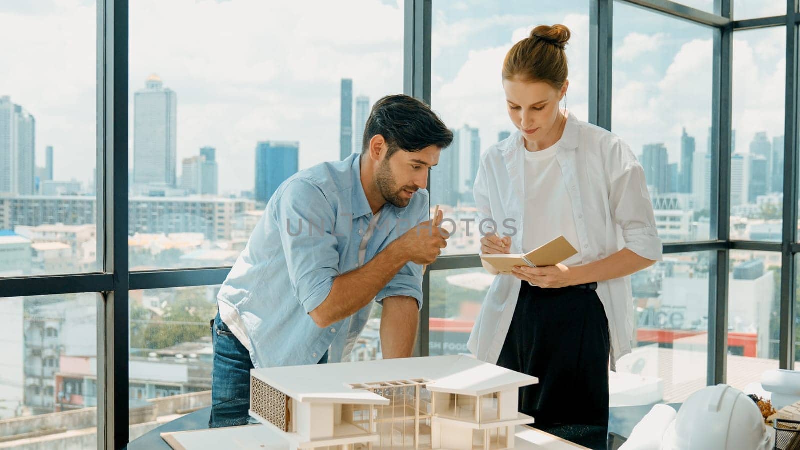 Skilled architect engineer team discussion about house model construction. Smart interior designer sharing, talking about building design while beautiful coworker taking a note. Design. Tracery