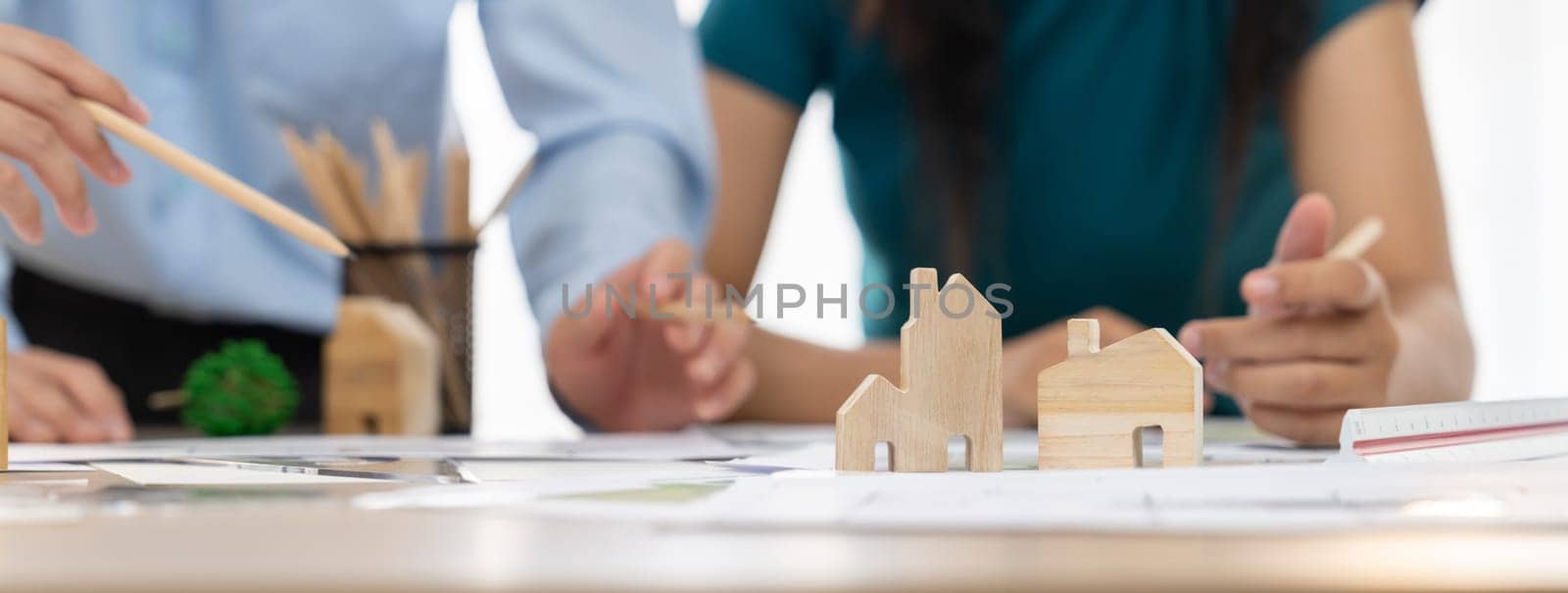 Professional architect engineer team discussion about architectural project on meeting table with wooden block and blueprint scatter around. Design and cooperate concept. Closeup. Delineation.