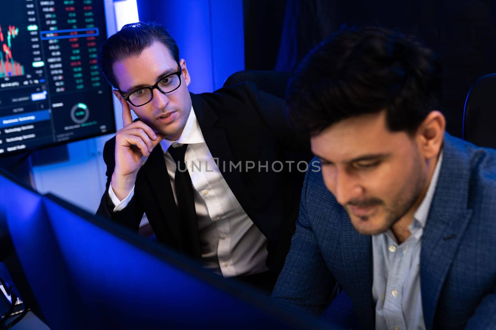 Two stock exchange traders discussing digital currency or market online focusing on dynamic data monitor. Concept of analyzing market stock cooperate at neon blue-light decorative workplace. Sellable.