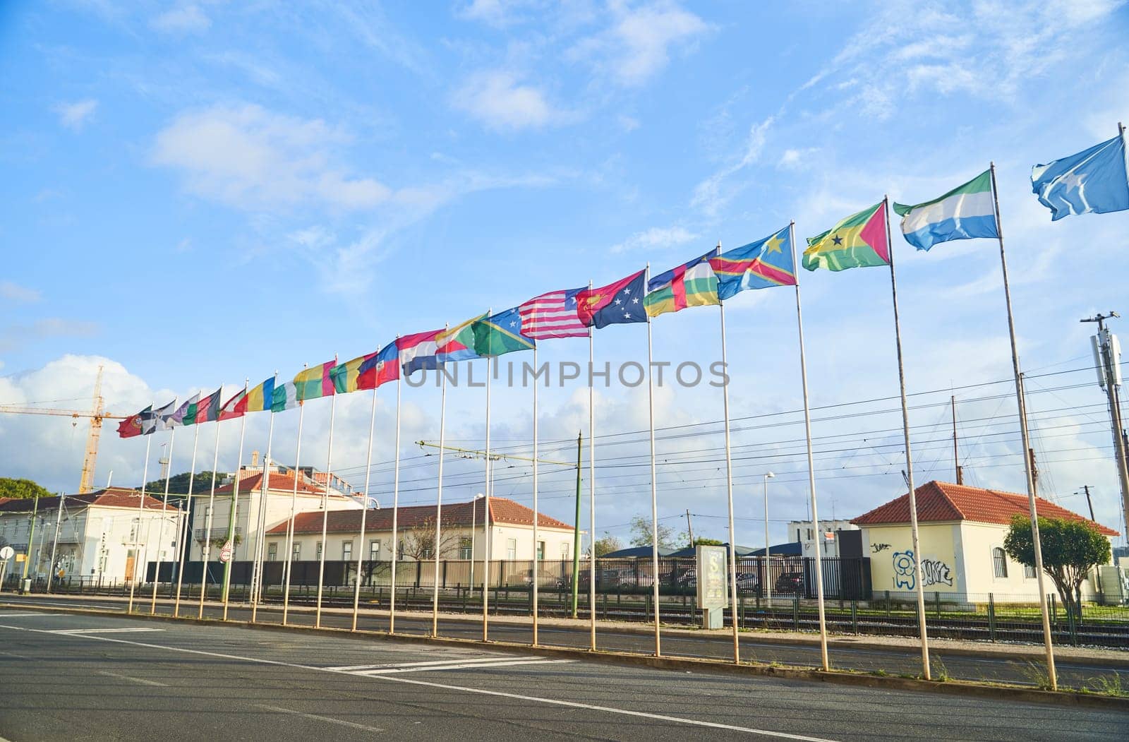 Flags hanged high in the air, fluttering against the cloudy sky, contrasting with the urban landscape of buildings and asphalt roads