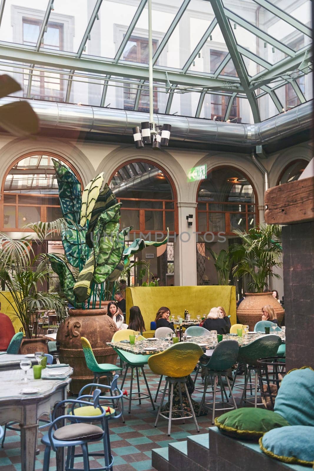 A restaurant with tables, chairs, and houseplants under a glass roof by driver-s