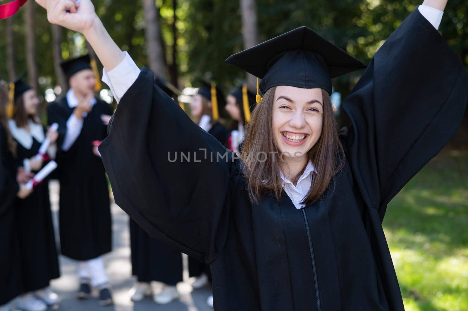 Group of happy students in graduation gowns outdoors. A young girl boasts of her diploma. by mrwed54