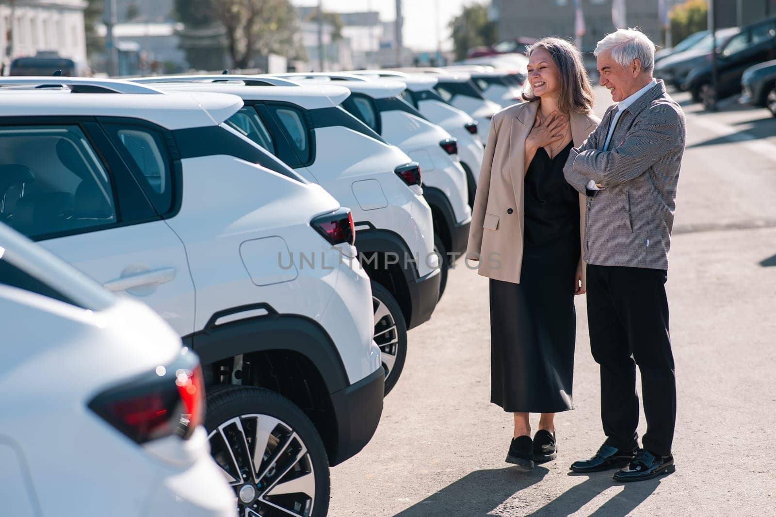 Mature Caucasian couple walks past cars outdoors, choosing a new one. by mrwed54
