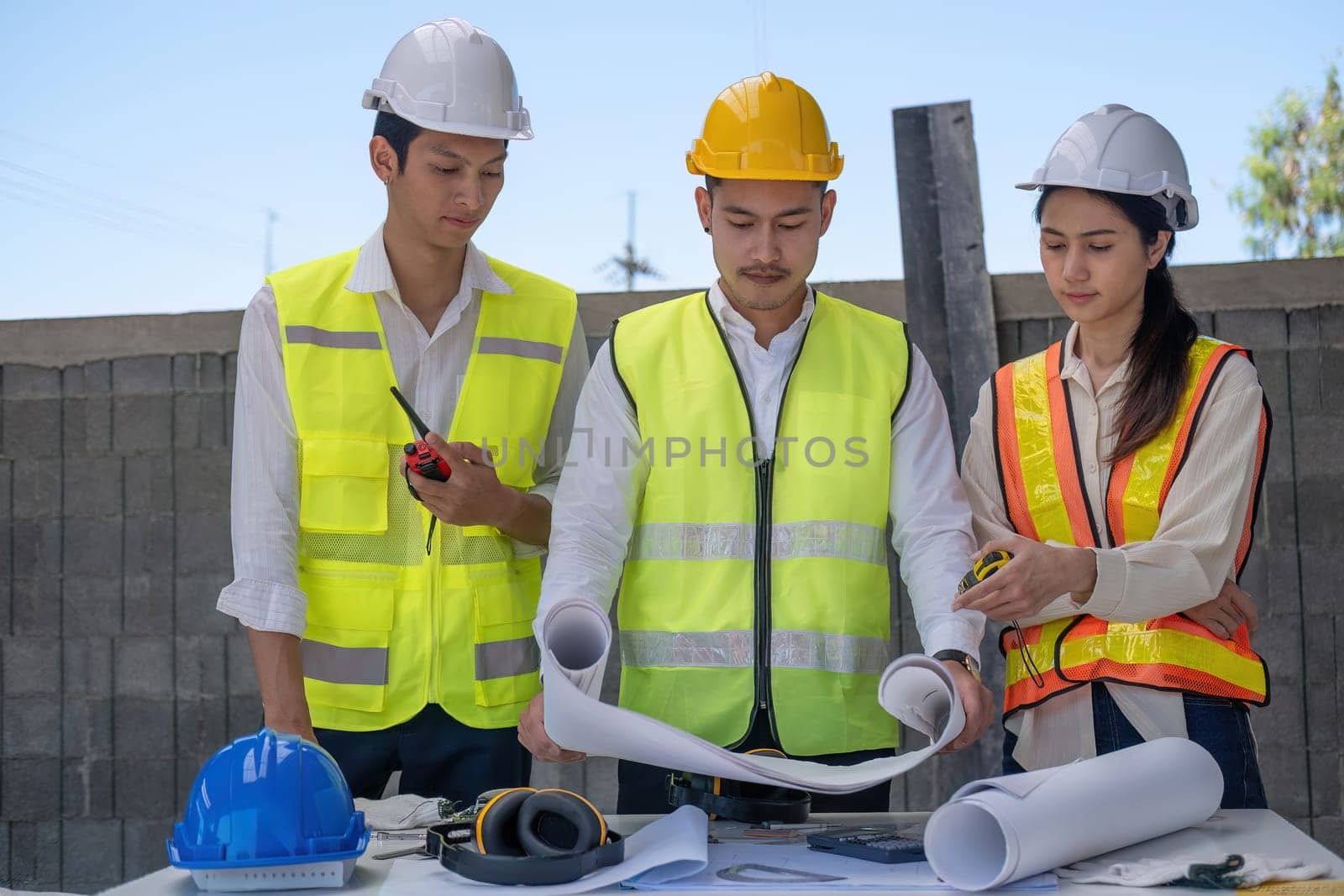 Civil engineer teams meeting working together wear worker helmets hardhat on construction site in modern city. Foreman industry project manager engineer teamwork. Asian industry professional team.