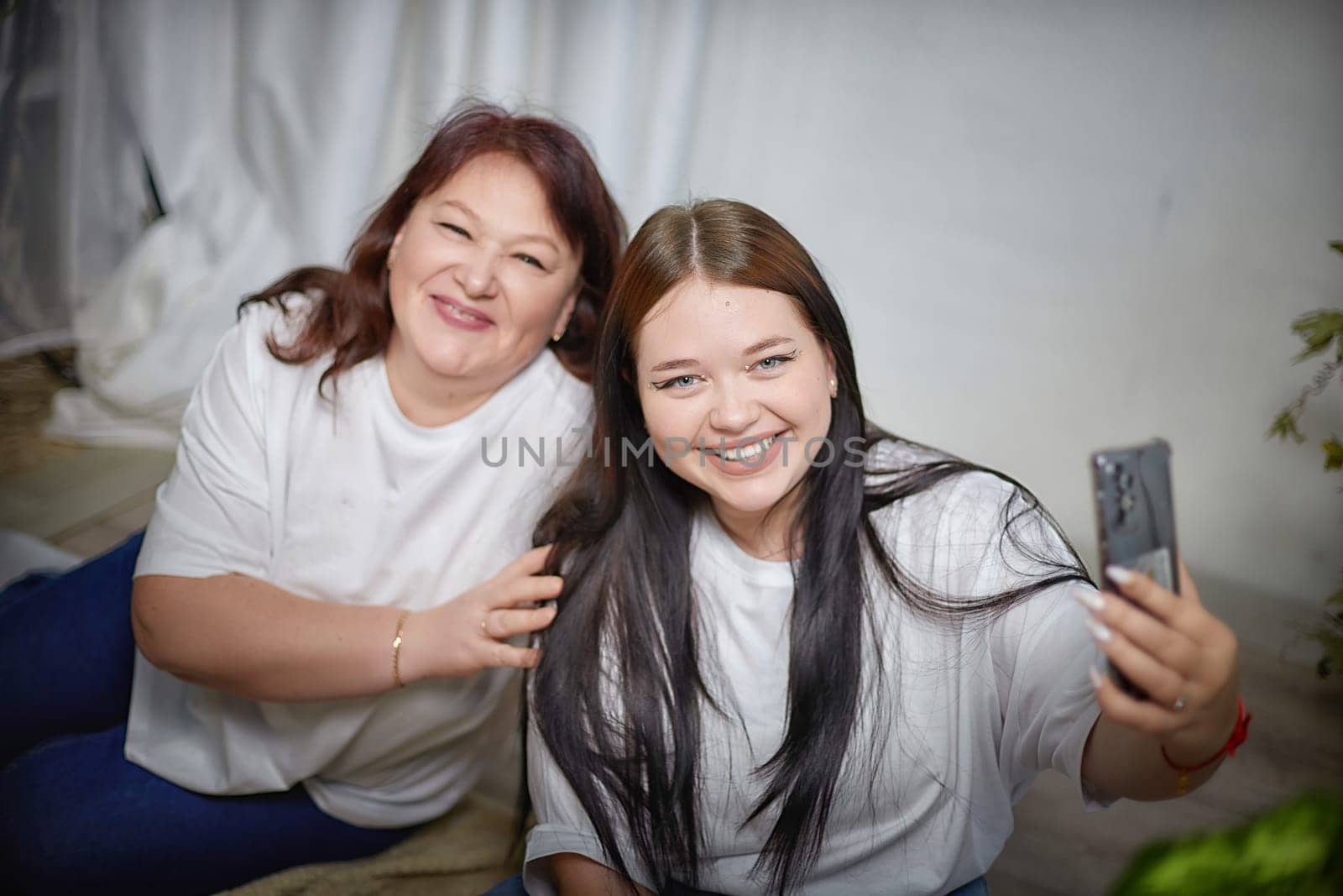 Fat funny funny adult mother and daughter posing, taking selfies indoors. Body positive, friendly family in the room